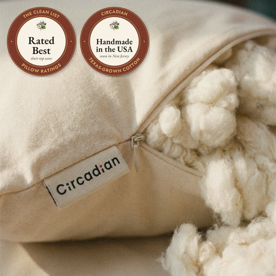 Close-up of the woven Circadian label beside the zipper of the Organic Cotton Pillow, with cotton spilling out, and two seals: rated Best by The Clean List, and handmade in the USA from Texas-grown cotton.