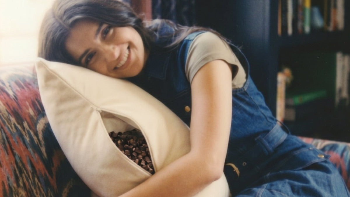 A smiling woman in denim overalls hugs her Circadian Buckwheat Pillow.