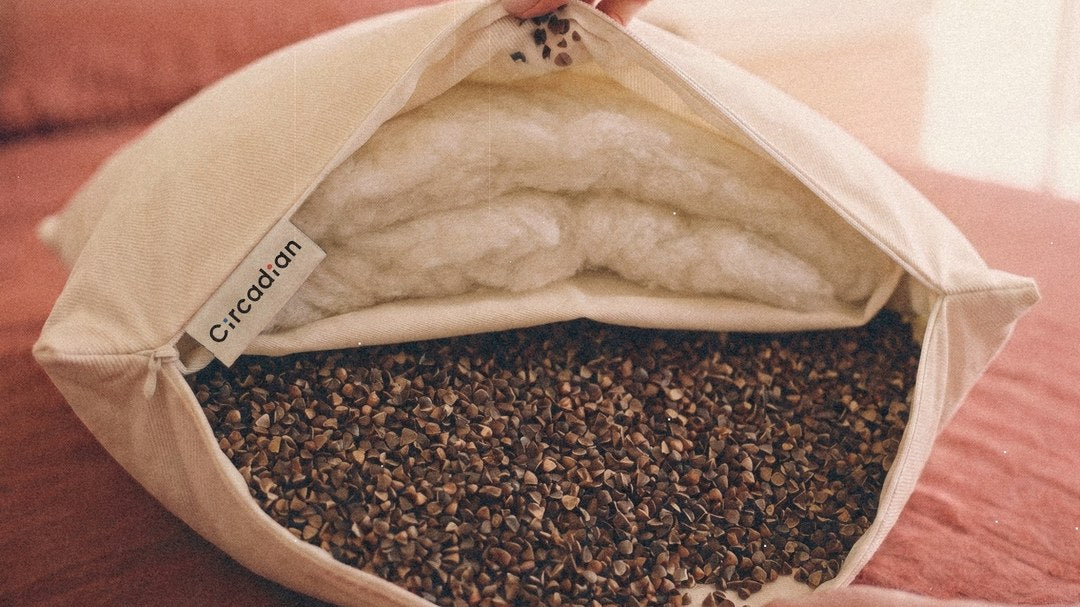An open Buckwool Hybrid Pillow on a bed: organic wool layers on one side, buckwheat hulls on the other