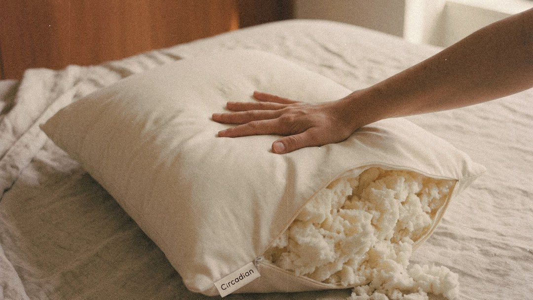 A hand presses a Tree-Tapped Latex Pillow on a made bed