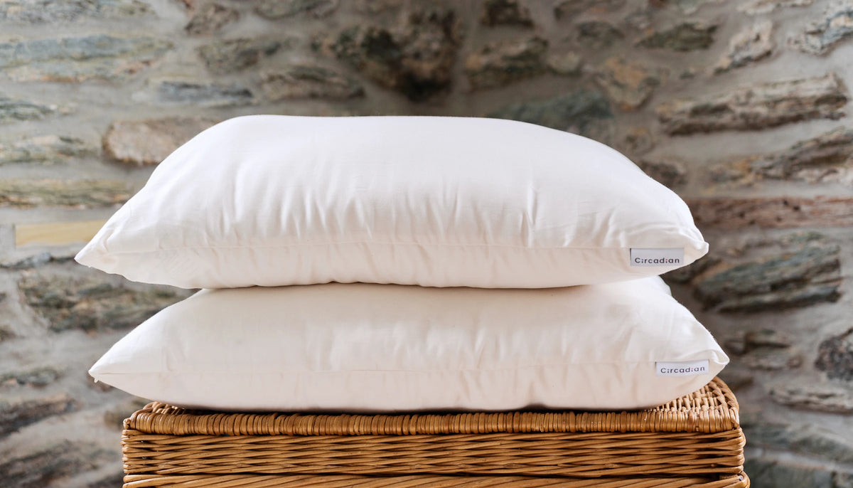 Two Circadian pillows stacked on a wicker basket against a stone wall.
