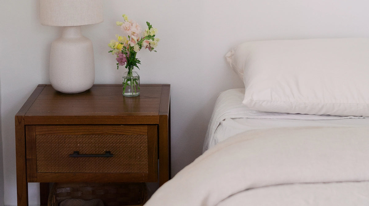 A Circadian pillow on a made bed beside a wooden nightstand with a lamp and flowers.