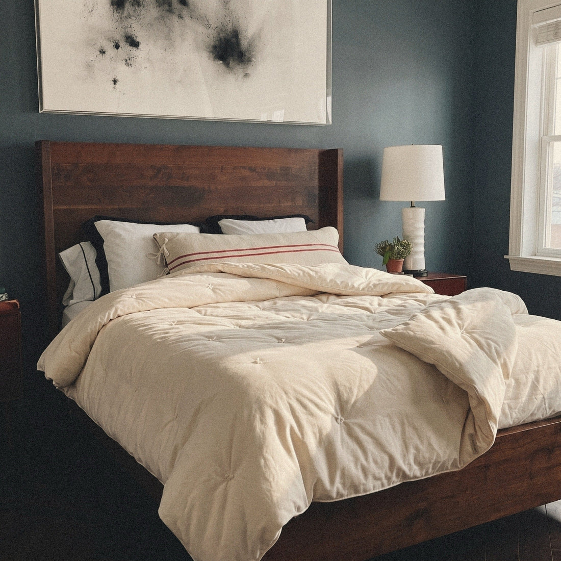 Morning sun on a dark wood bed. The Circadian Organic Wool Comforter, a hand-tufted duvet insert, lies thrown back across it.