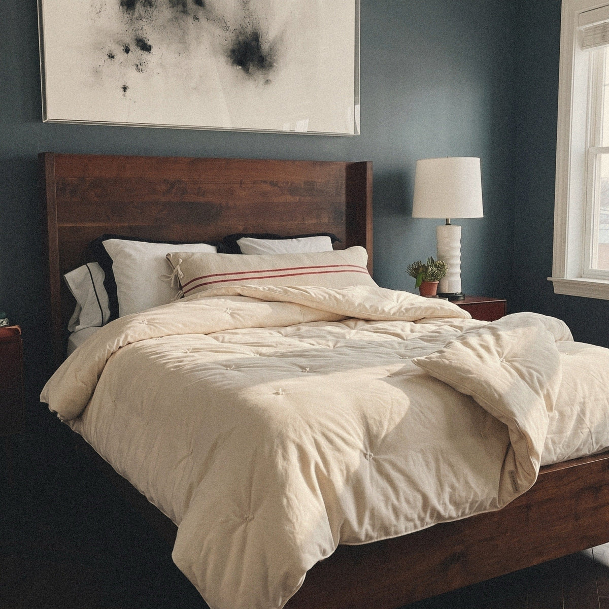 Morning sun on a dark wood bed. The Circadian Organic Wool Comforter, a hand-tufted duvet insert, lies thrown back across it.