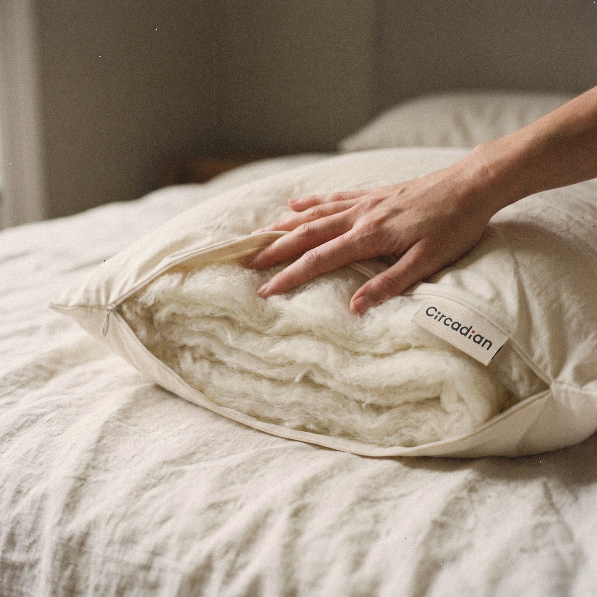 A hand presses into the soft layers of wool at the open end of the Circadian Organic Wool Pillow.