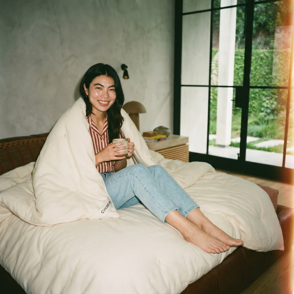 Woman wrapped in Circadian Organic Wool Duvet on leather daybed with mug, GOTS-certified wool fill