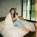 Woman wrapped in Circadian Organic Wool Duvet on leather daybed with mug, GOTS-certified wool fill