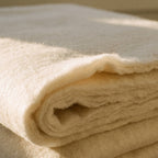 Close view of washable merino wool batting, a folded sheet showing its layers and soft torn edge