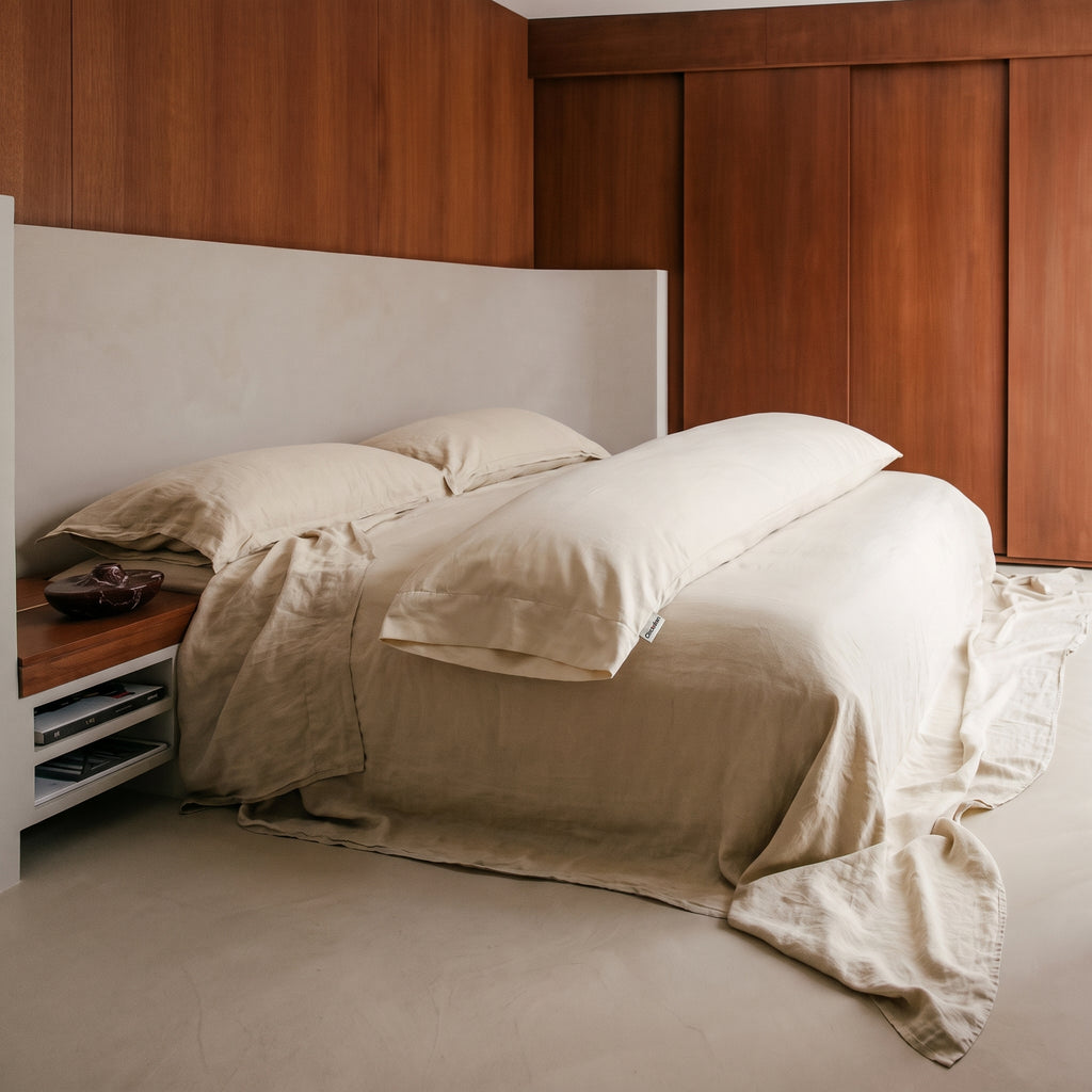 A body pillow in an organic cotton case lying along a made bed