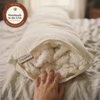 A hand rests on the soft organic cotton inside the open end of the Circadian Body Pillow, its woven label sewn beside the zipper, with a seal: handmade in the USA from Texas-grown cotton.