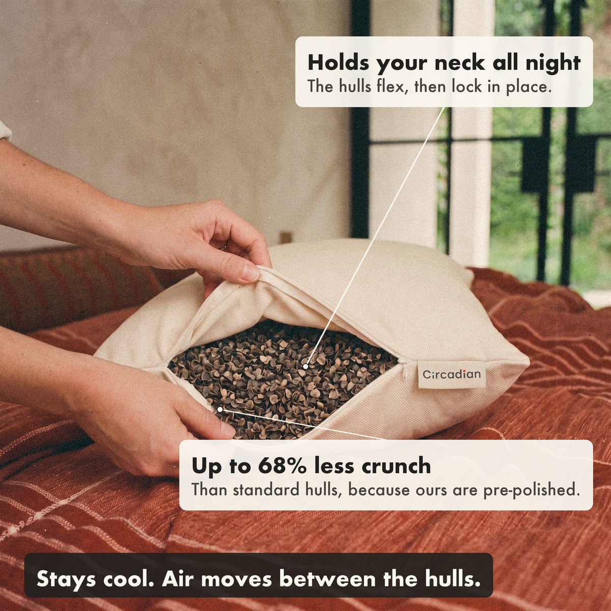Hands open the zipper of the Buckwheat Pillow on a bed to show the hulls inside, with labels: holds your neck all night, up to 68% less crunch than standard hulls, stays cool.