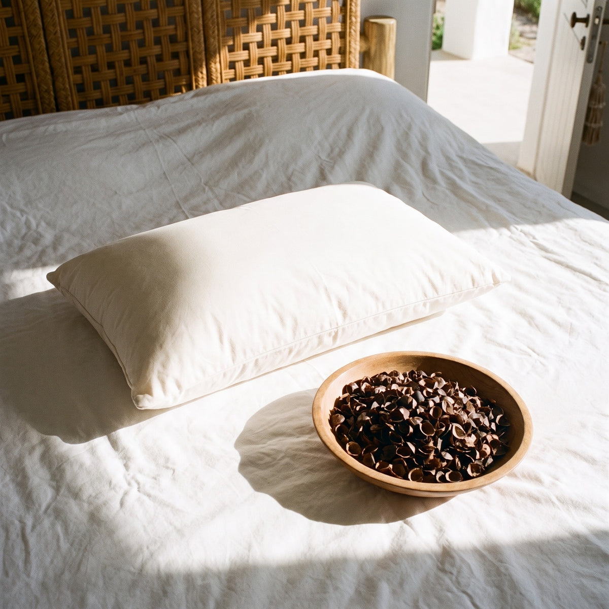 Circadian Buckwheat Pillow zipped closed on a white sheet, with a small wooden bowl of its dark buckwheat hulls beside it.