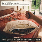 A hand pours buckwheat hulls back into the Buckwool Hybrid Pillow. The labels say up to 68% less crunch than standard hulls, because ours are pre-polished, with hulls grown in the USA and wool from New Zealand.
