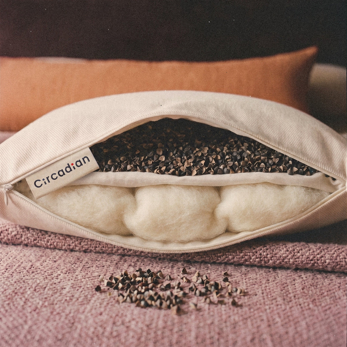 Close-up of the woven Circadian label beside the open zipper of the Buckwool Hybrid Pillow, a layer of buckwheat hulls above a cotton divider and a layer of wool below.