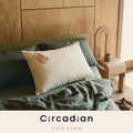 Circadian Gift Card: our cream organic cotton pillow with a kraft-paper gift tag on an unmade green linen bed