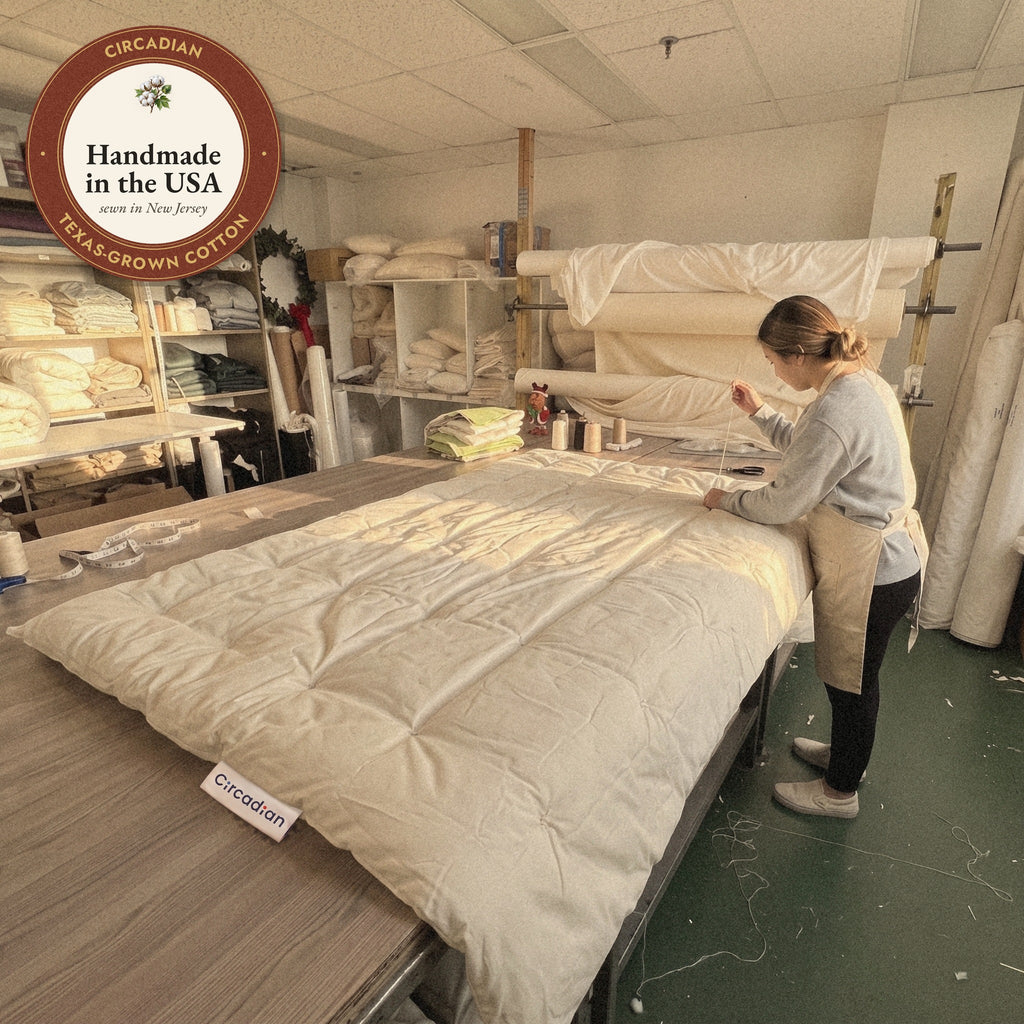 In the New Jersey workshop where it is made, a worker ties the tufts of an Organic Cotton Comforter by hand, shown with our Handmade in the USA seal.