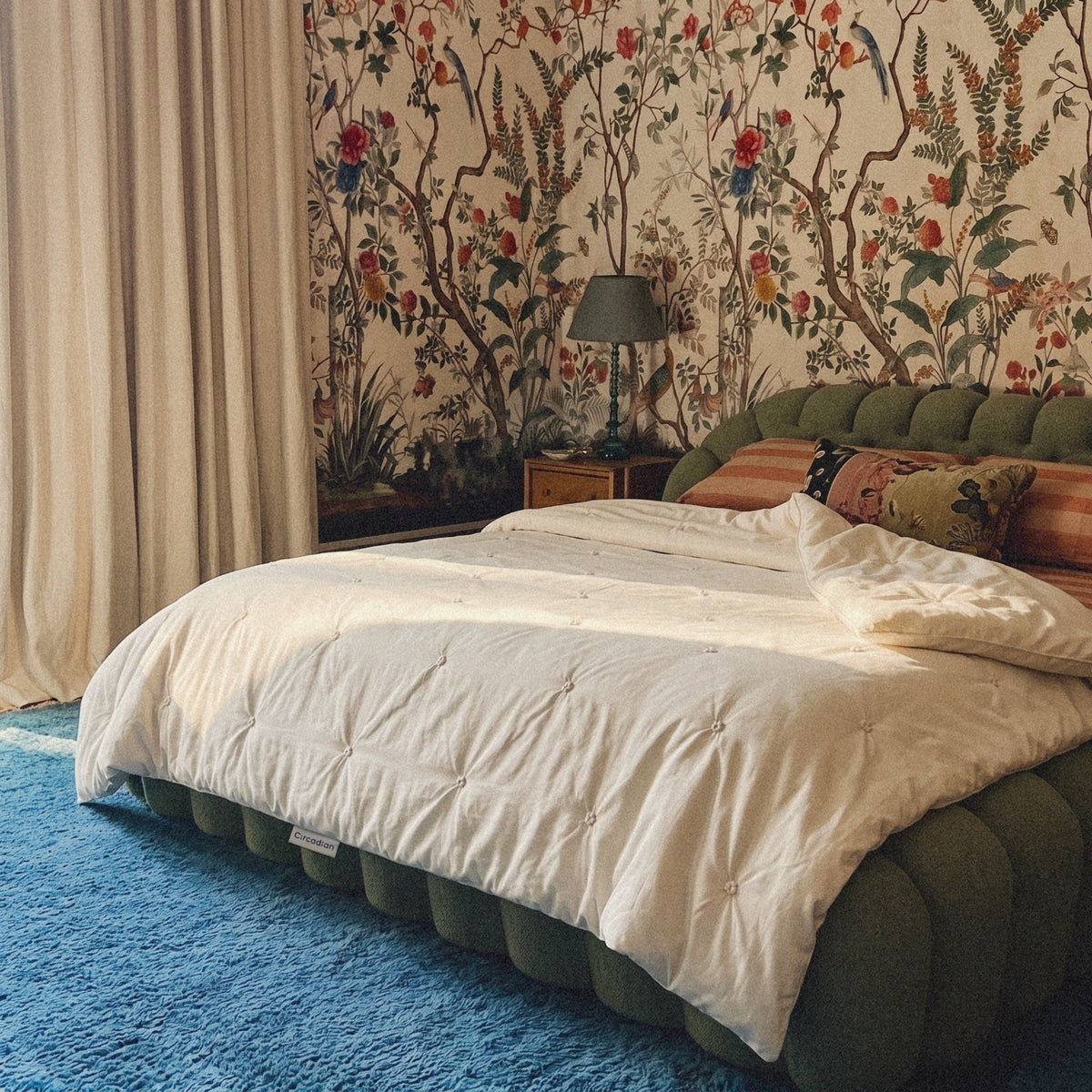 Our Organic Cotton Comforter on a green bed in front of a floral mural, its woven Circadian label at the edge.