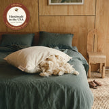 Our Wild-Harvested Kapok Pillow on a green linen bed. Soft, fluffy kapok spills from the open zipper.