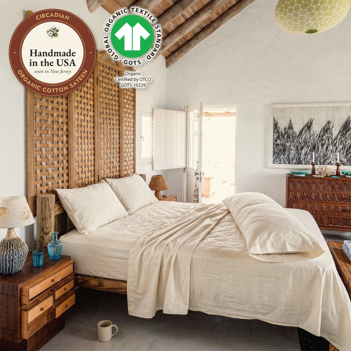 A body pillow in a Circadian organic cotton sateen body pillow case along a bed in a beamed bedroom, with seals: handmade in the USA from organic cotton sateen, and the GOTS organic label.