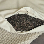 A hand opens the zipper of the Circadian Buckwheat Pillow and scoops through the small, dark buckwheat hulls inside.