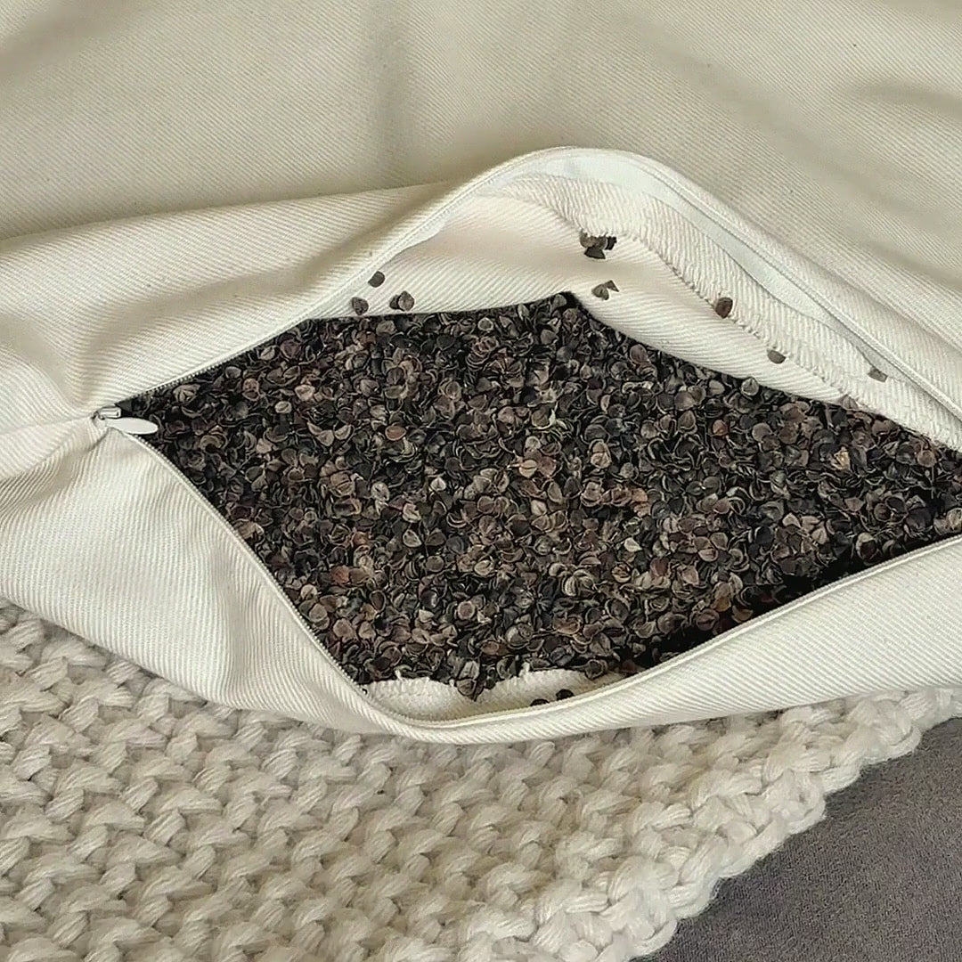 A hand opens the zipper of the Circadian Buckwheat Pillow and scoops through the small, dark buckwheat hulls inside.