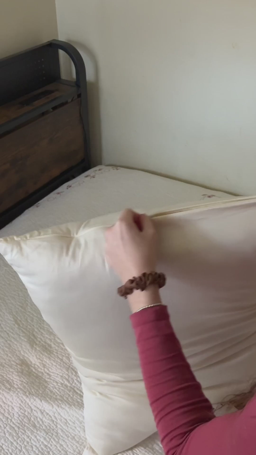 A woman unzips her Organic Wool Pillow, presses into the layers of wool inside, then hugs the pillow on her bed.