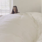 On a rainy day, a woman makes the bed with the Circadian organic comforter, then settles in under it with a book.