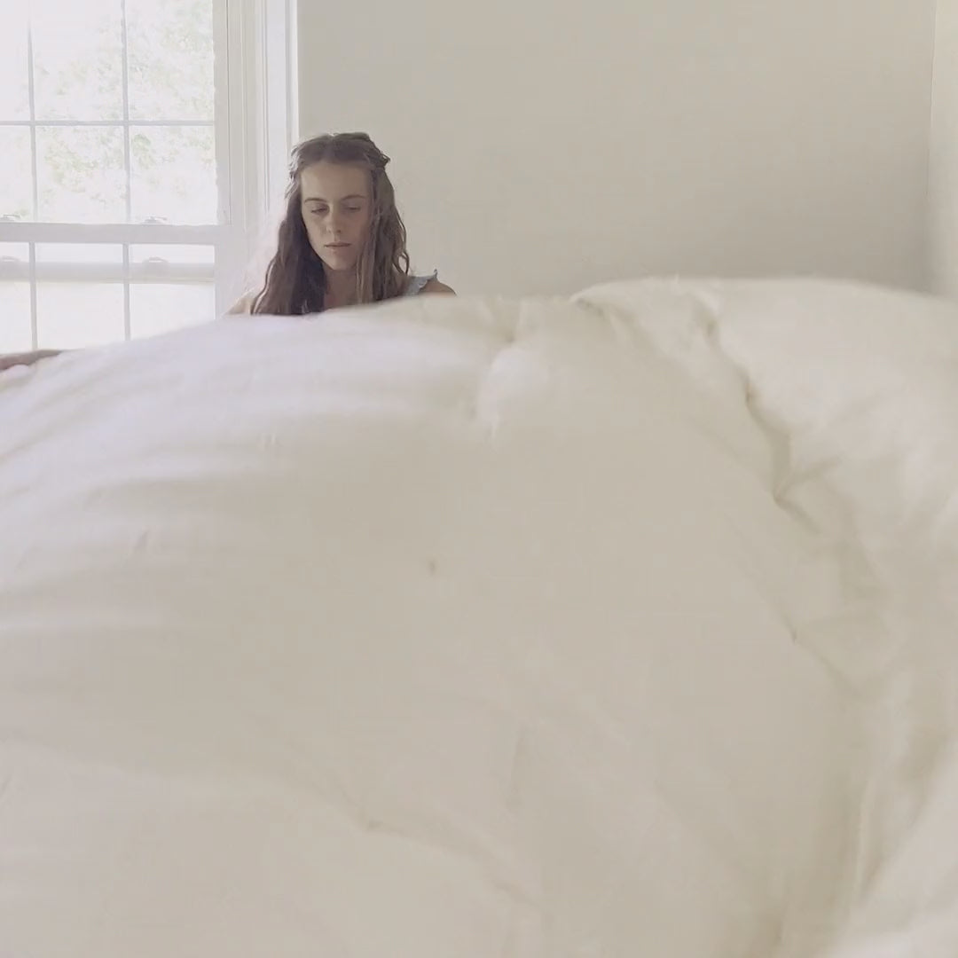 On a rainy day, a woman makes the bed with the Circadian organic comforter, then settles in under it with a book.