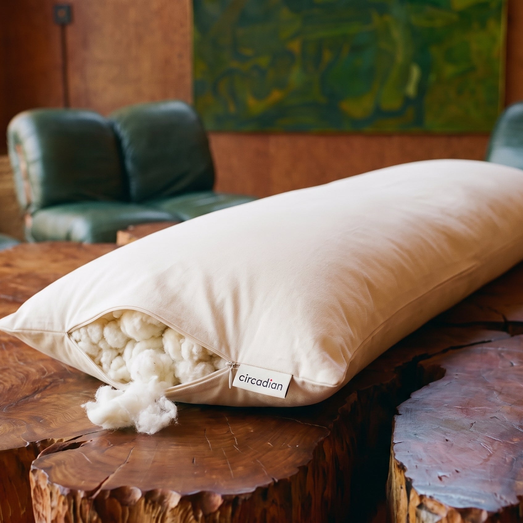 Circadian Body Pillow on a live-edge redwood table, organic cotton fill spilling from the open side zipper, brand tag visible.