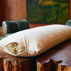 Circadian Body Pillow on a live-edge redwood table, organic wool fill spilling from the open side zipper.