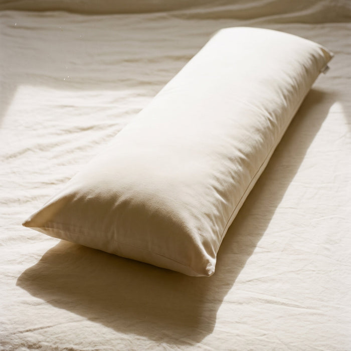 Circadian Body Pillow in a cream organic cotton cover resting lengthwise across a made bed, morning light.