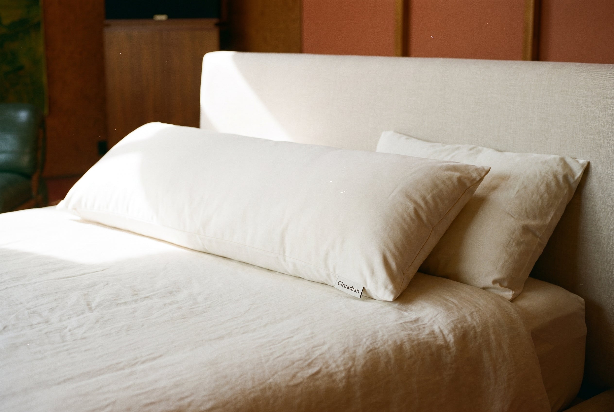 Full-length Circadian Body Pillow lying across a made bed beside a standard pillow, showing its roughly 20 by 72 inch length.