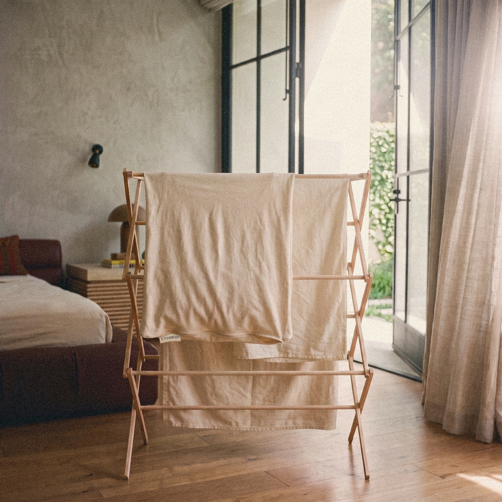 An empty waterproof organic cotton pillow protector drying flat on a wooden rack after a cold wash.