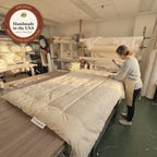 In the New Jersey workshop where it is made, a worker ties the tufts of an Organic Wool Comforter by hand, shown with our Handmade in the USA seal.