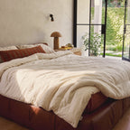 Our Organic Wool Comforter thrown back on a leather bed in a bright plaster bedroom with doors open to the garden, its woven Circadian label at the edge.