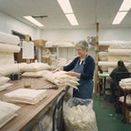 A woman in our New Jersey workshop slides soft layers of carded wool batting into an organic cotton pillow cover by hand.