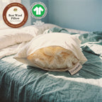 A Circadian Organic Wool Pillow on a teal blanket in morning sun, its end unzipped to show soft layers of wool batting inside, with The Good Trade seal (best wool pillow, best for allergy-resistant wool) and the GOTS label: Organic, certified by OTCO, GOTS-10229.