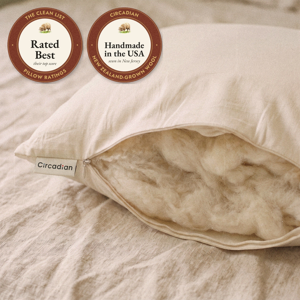 Close-up of the open corner of the Organic Wool Pillow beside its woven Circadian label, showing soft, airy wool inside, with two seals: rated Best by The Clean List, and handmade in the USA from New Zealand-grown wool.